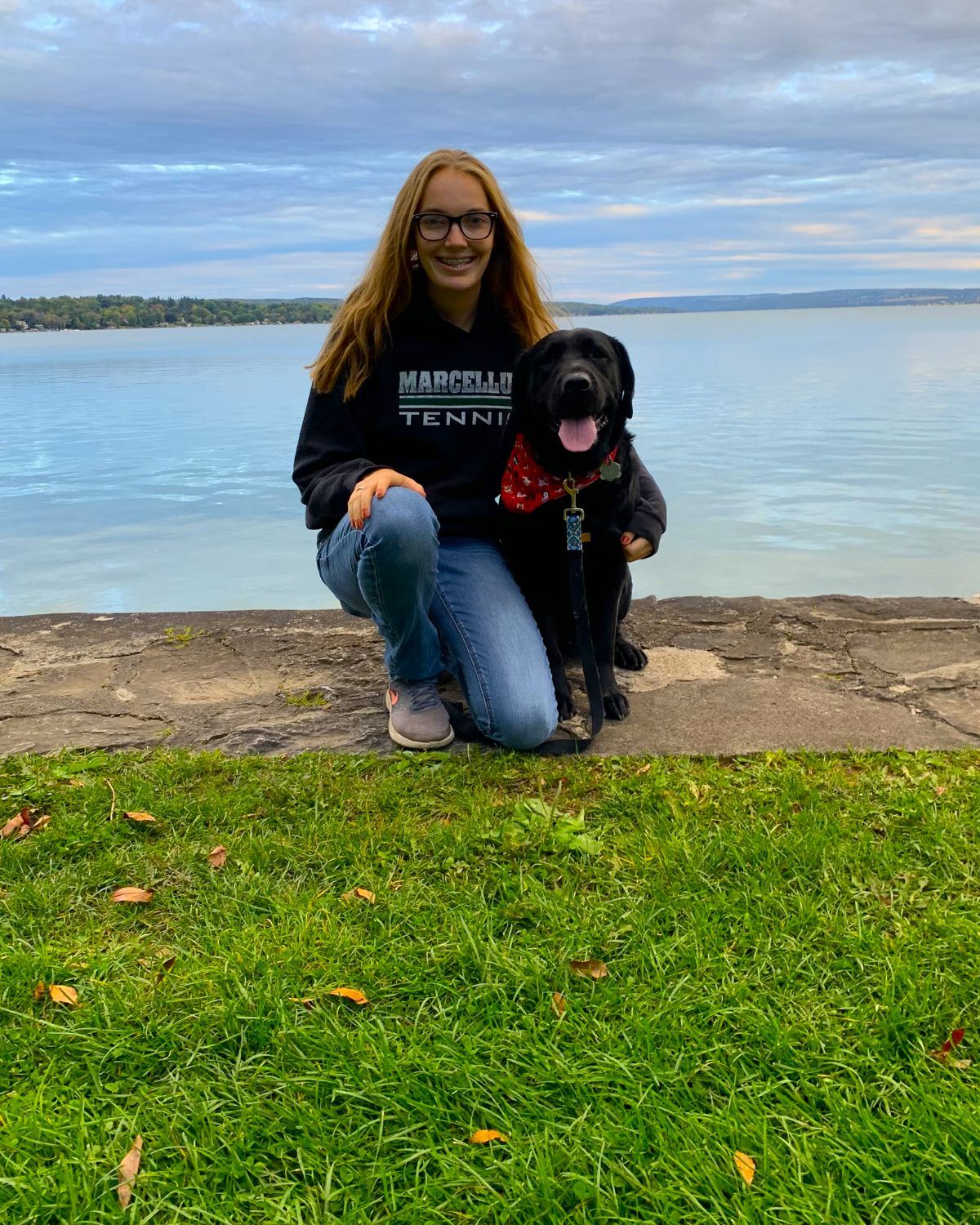 Madi from Lloyd's Neighborhood Pet Sitting with a happy black Labrador by the lake